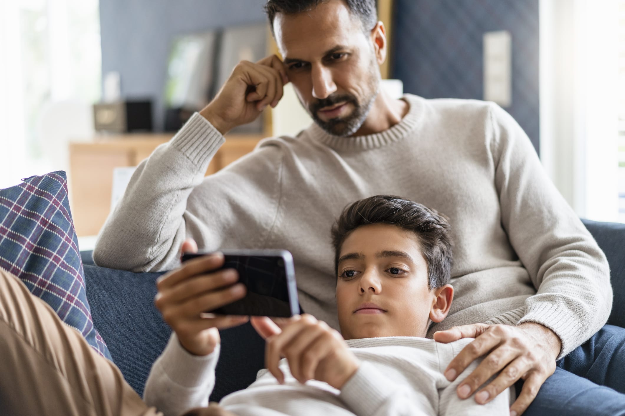 Father and son using smartphone on couch in living room