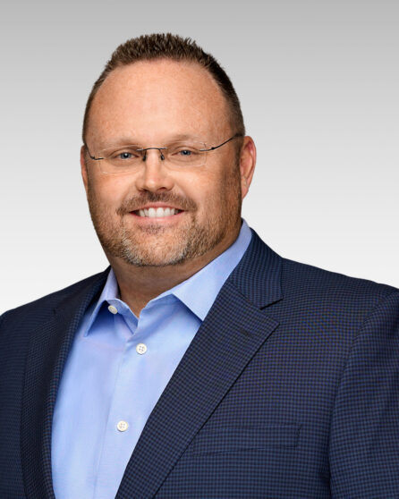 A man wearing glasses in a blue suit smiling at the camera.