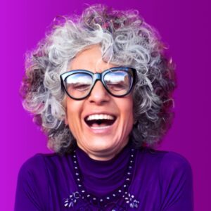 A grey-haired woman smiling against a vibrant purple background.