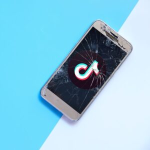 A cracked phone screen on a split blue background. The TikTok logo is on the screen.