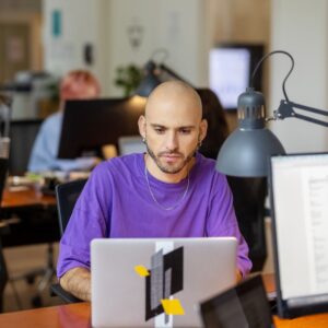 A man in a purple shirt working at a computer