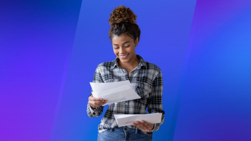 A woman smiling and reading mail in front of a blue background