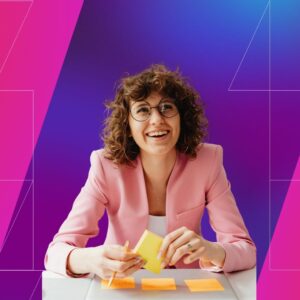 A woman in a pink suit jacket holding post-its. She's in front of a pink and purple geometric background.