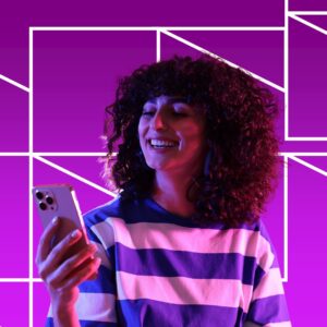 A young woman in a blue and white sweater looking at her phone in front of an angular purple background