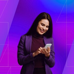 A woman in a purple blazer and sweater smiling down at her phone. She stands in front of a pink and purple ombre background with a geometric pattern.