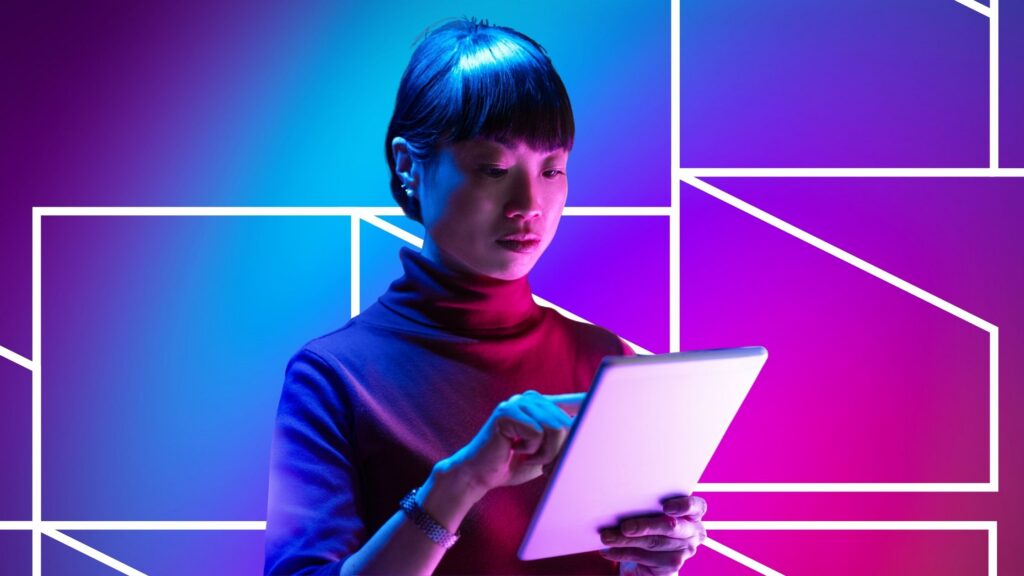 A woman uses a tablet with a focused expression, illuminated by blue and pink lighting against a vibrant blue, pink, and purple background with geometric line patterns, suggesting digital interaction and modern technology use.