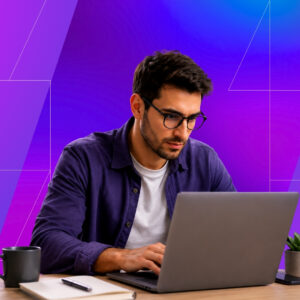 A man wearing glasses works on a laptop at a desk with a notebook and coffee mug, set against a vibrant purple and blue geometric background.